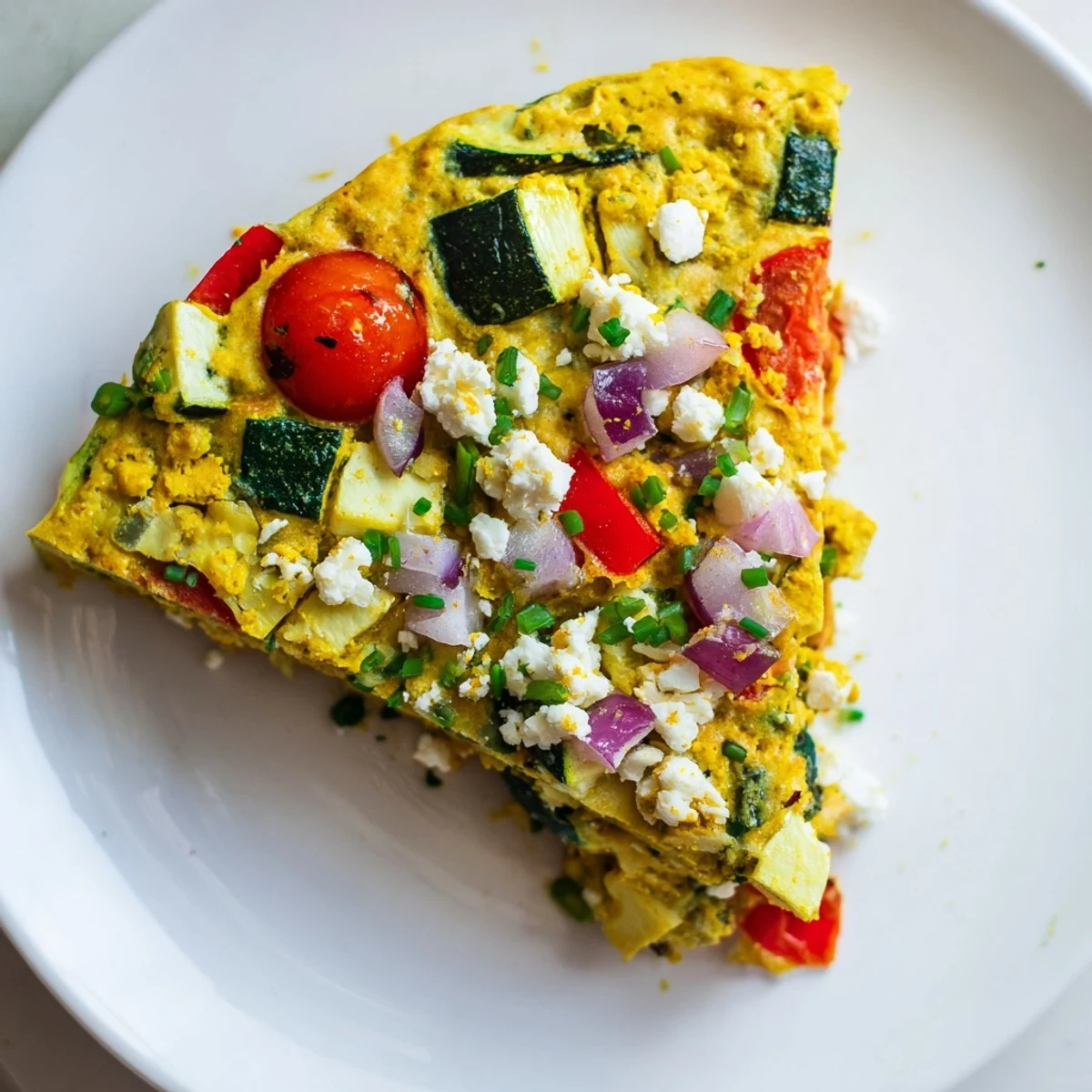Sliced wedge of New Year Vegan Frittata served on a white plate, topped with crumbled vegan feta and fresh chives.