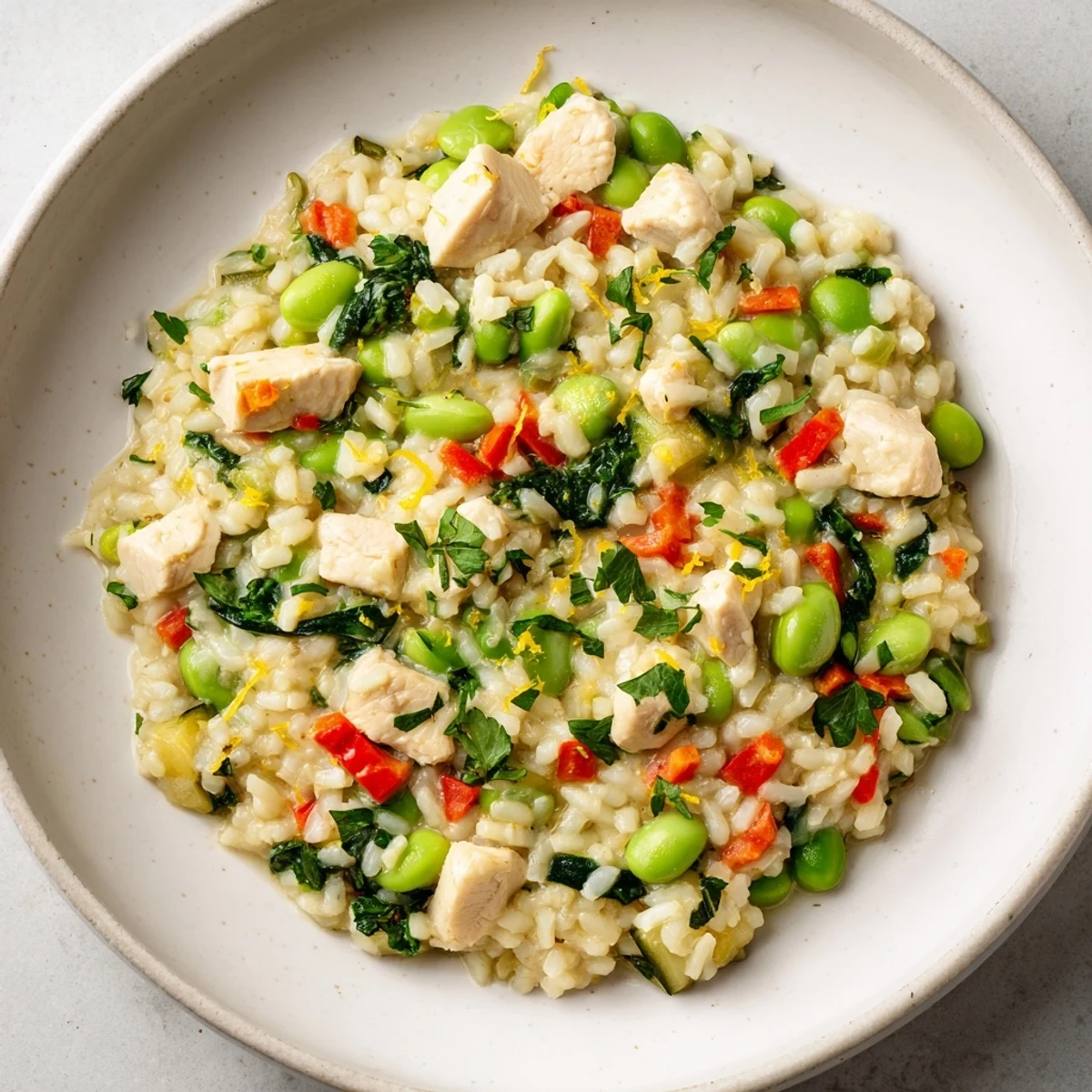 Creamy Solstice High Protein Risotto with chicken, peas, and edamame, garnished with fresh parsley and lemon zest.