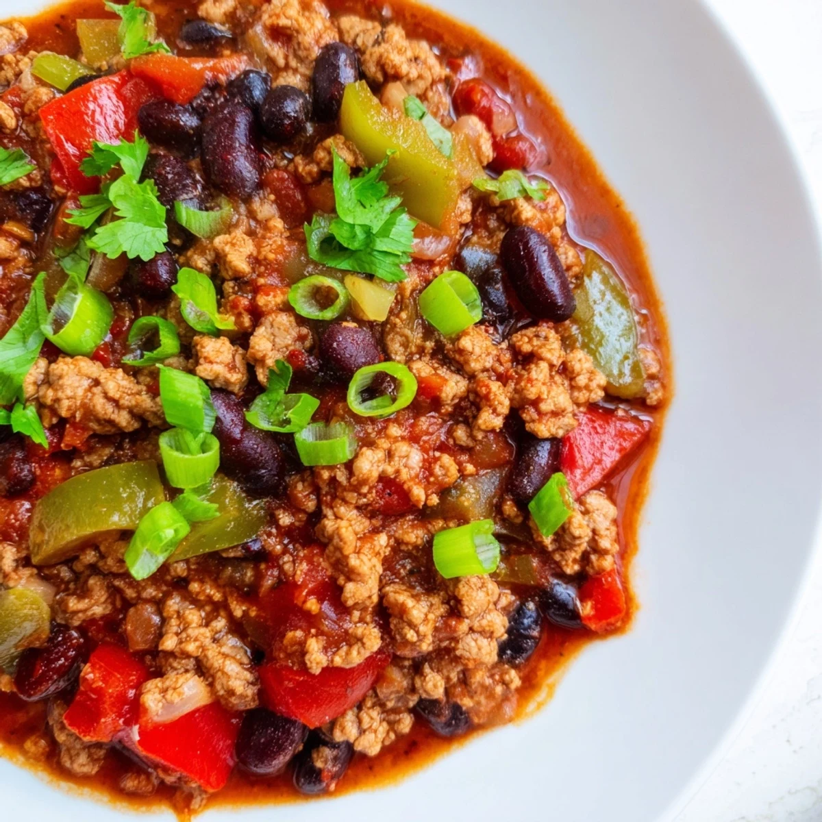 Spoon a serving of Crisp Air High Protein Chili topped with green onions and cilantro into a rustic bowl.