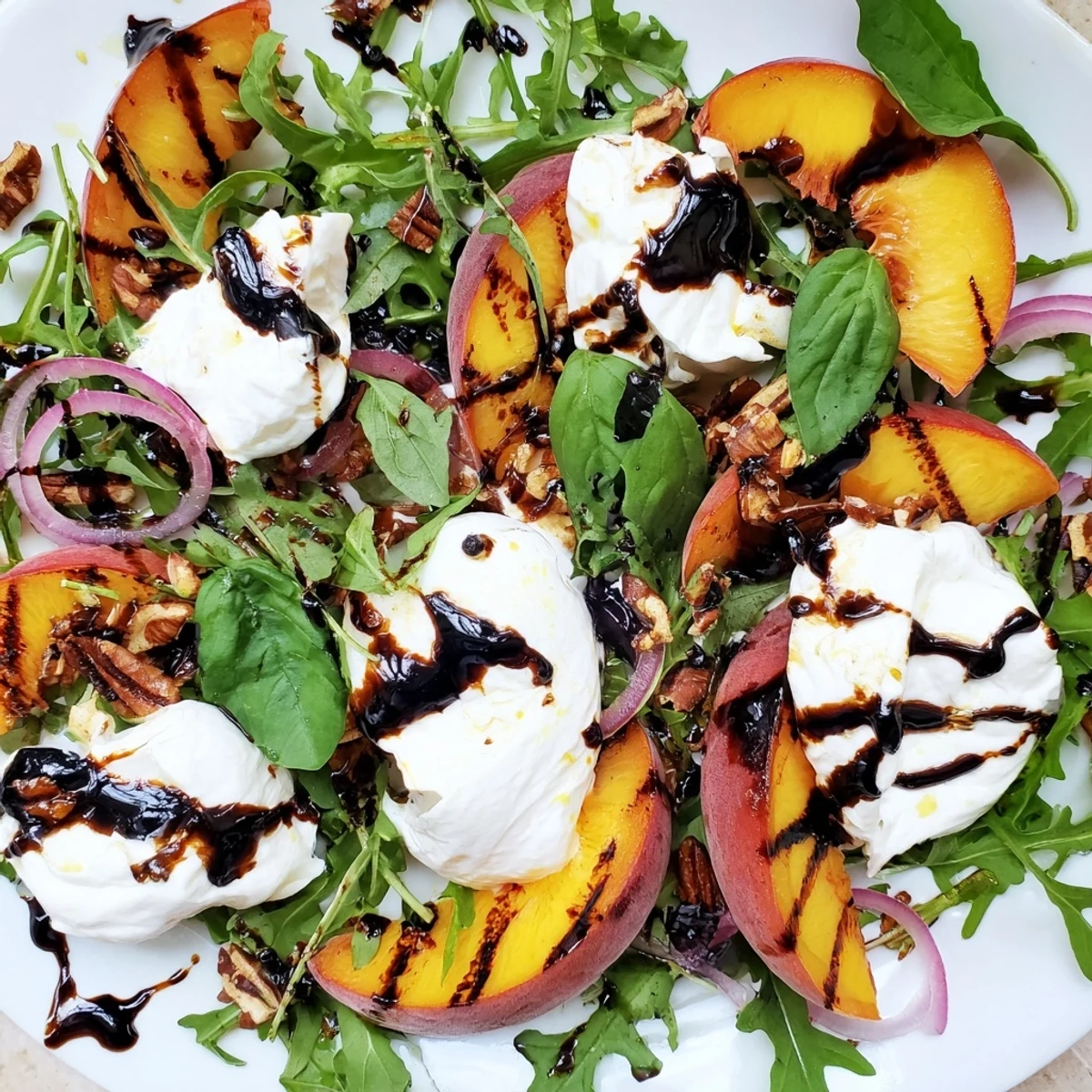 A close-up view of the Grilled Peach and Burrata Arugula Salad, showing golden grill marks on fruit and fresh basil garnish.