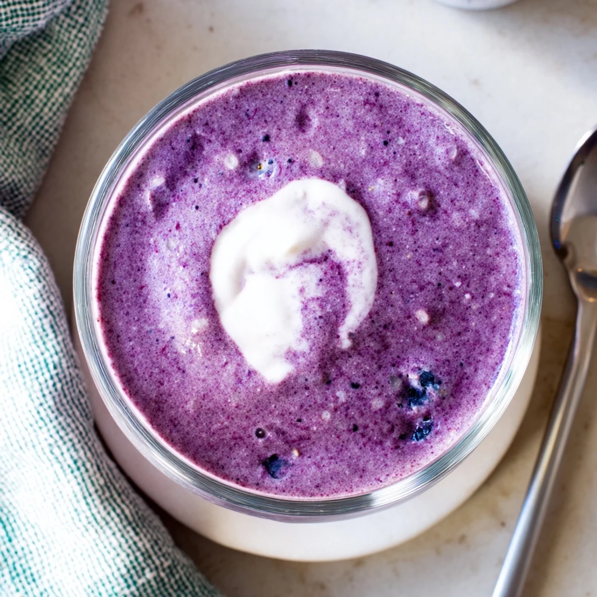 Blueberry almond butter protein smoothie being poured into a tall glass after blending to a velvety texture.