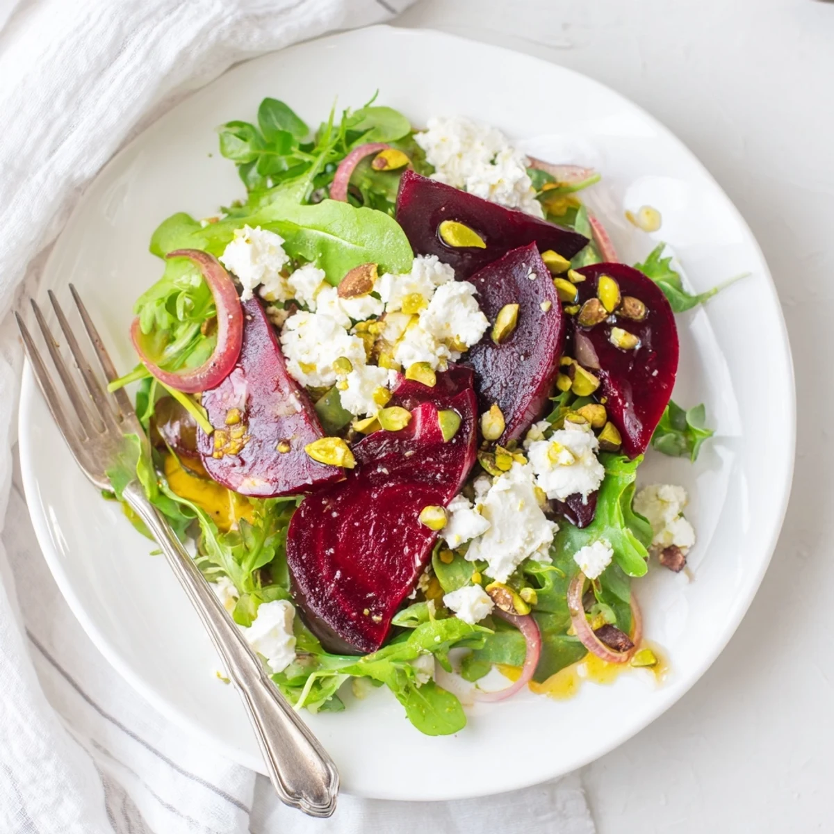 Vivid roasted beet and pistachio salad with citrus dressing on a platter, topped with creamy goat cheese and fresh greens.