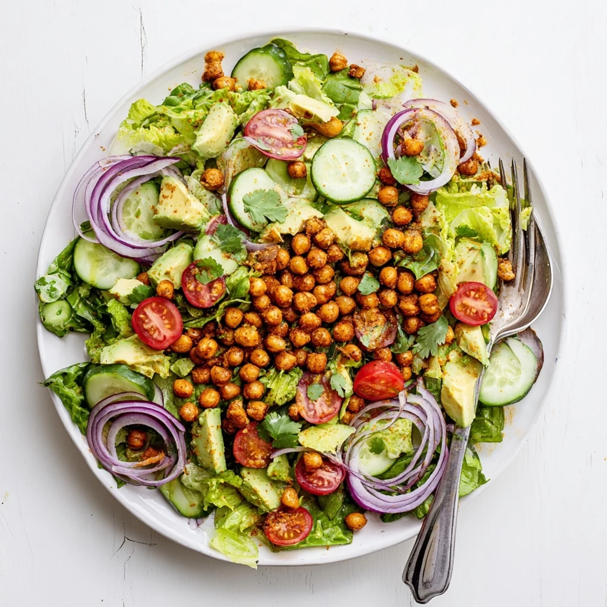 Colorful bowl of roasted spiced chickpeas atop creamy avocado and crisp vegetables in light salad arrangement