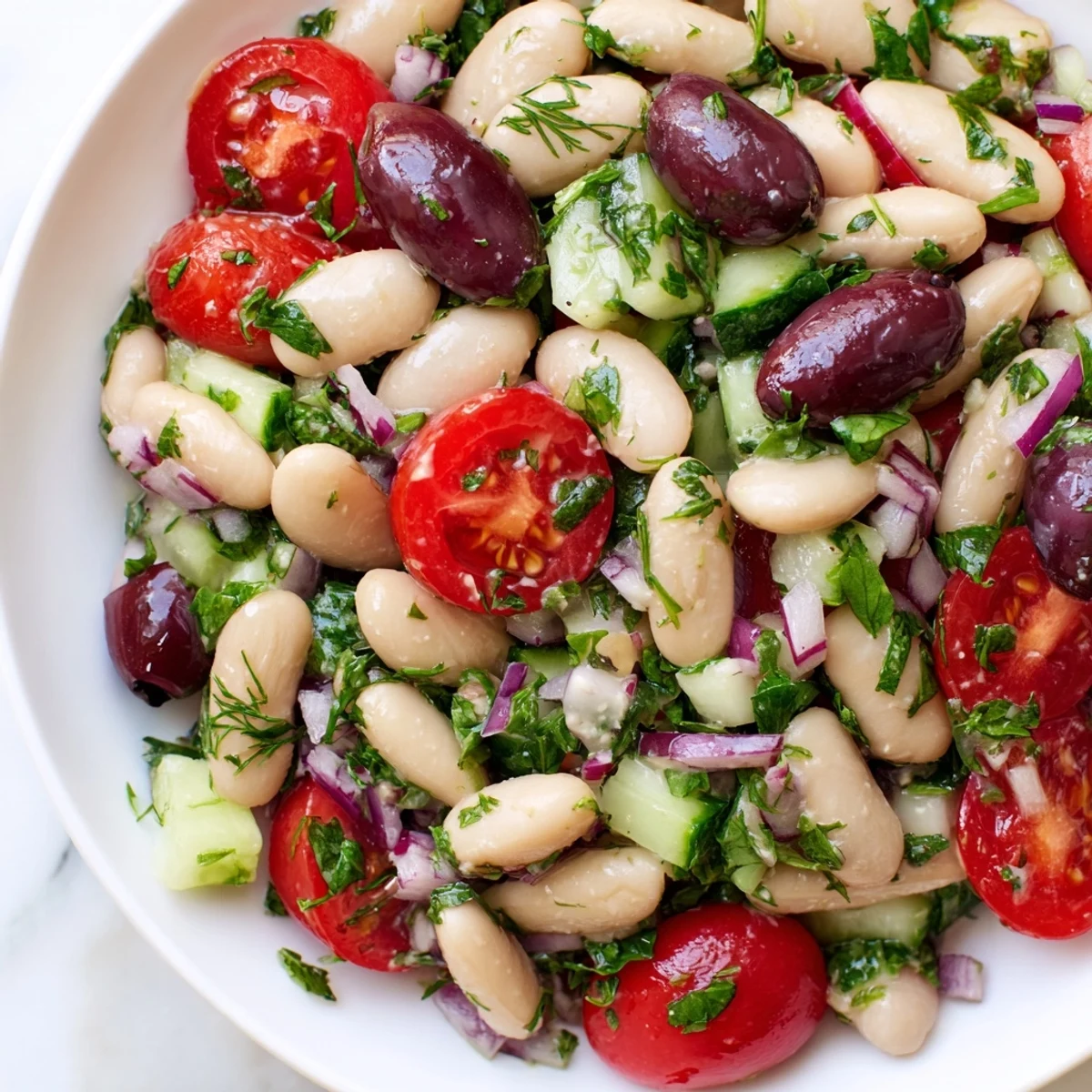 Colorful Mediterranean white bean and olive herb salad with fresh vegetables and zesty lemon dressing in a white bowl