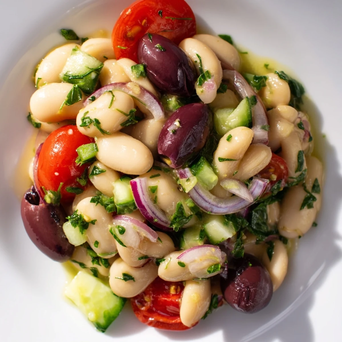 Protein-packed Mediterranean white bean and olive herb salad featuring crisp vegetables and bright green parsley, dill, and mint garnish
