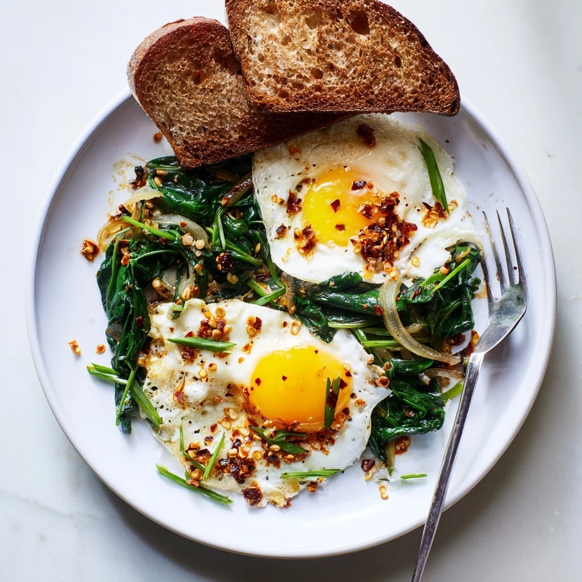 Sunny-side-up eggs sizzle in aromatic chili oil creating crispy lacy whites served over tender sautéed garlic spinach for a spicy breakfast