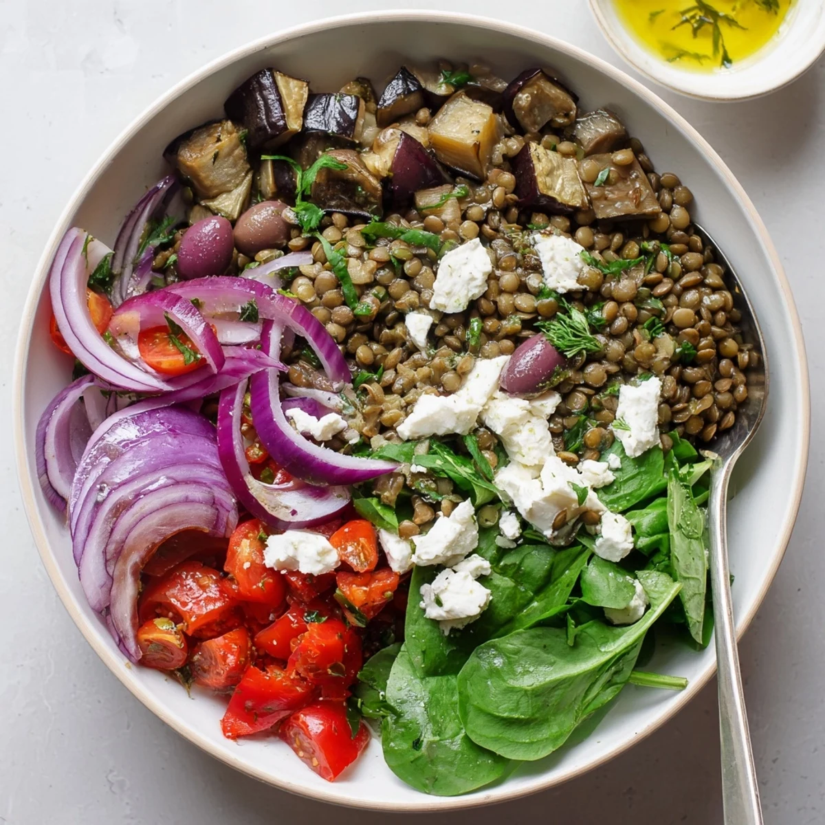 Colorful Mediterranean lentil and roasted eggplant bowl topped with feta, olives, and fresh parsley