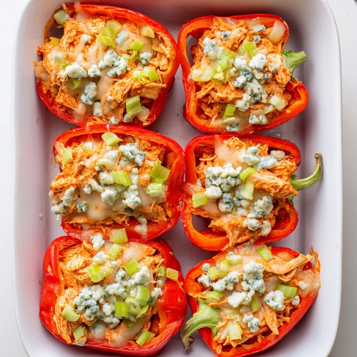Red bell peppers loaded with creamy buffalo chicken mixture bubbling in baking dish