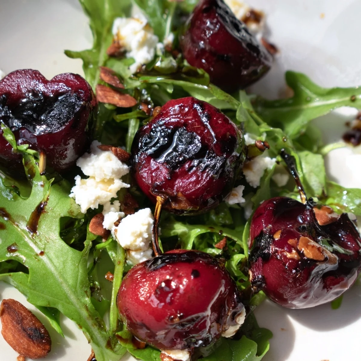 Fresh summer salad featuring charred cherries peppery arugula and crunchy almond topping on white plate