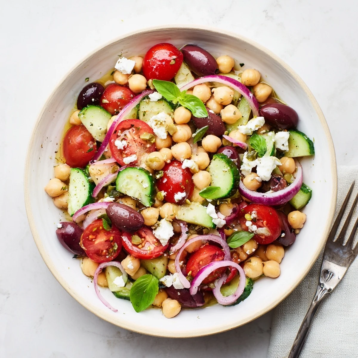 Colorful Mediterranean chickpea and tomato basil salad with fresh vegetables in a white serving bowl