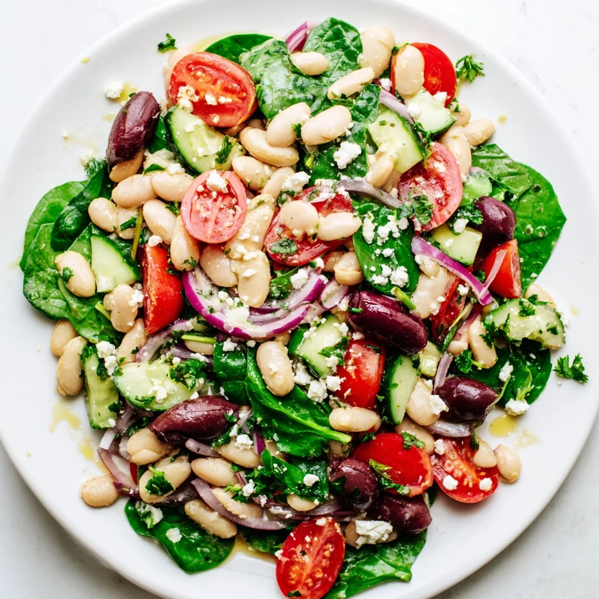 Creamy white bean spinach salad topped with bright red tomatoes, olives, and crumbled feta cheese on a rustic wooden table