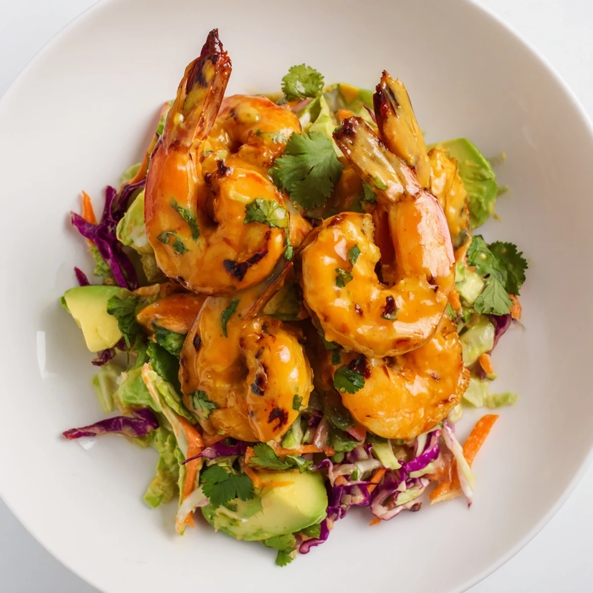 Golden spicy mango shrimp nestled on vibrant avocado lime slaw with fresh cilantro garnish