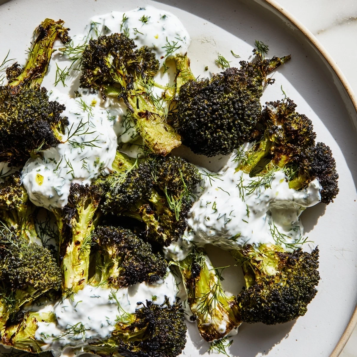 Golden roasted broccoli with lemon herb yogurt drizzle served on a rustic white platter