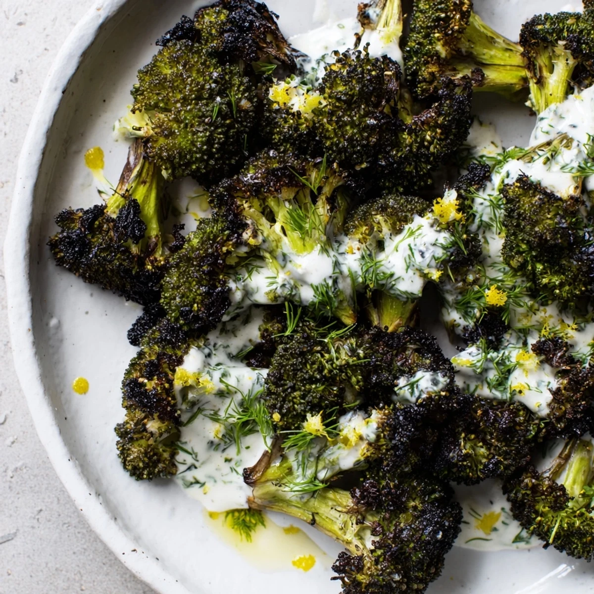 Bright green roasted broccoli with lemon herb yogurt drizzle garnished with fresh dill