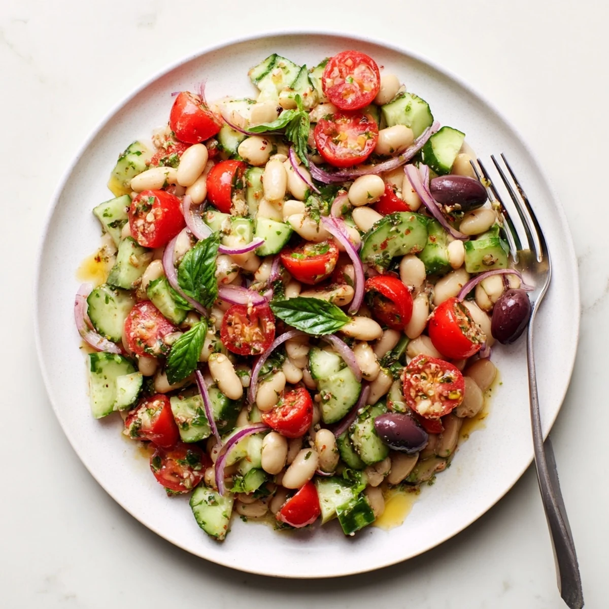 Vibrant Mediterranean white bean and tomato cucumber basil salad in a glass bowl garnished with fresh basil leaves