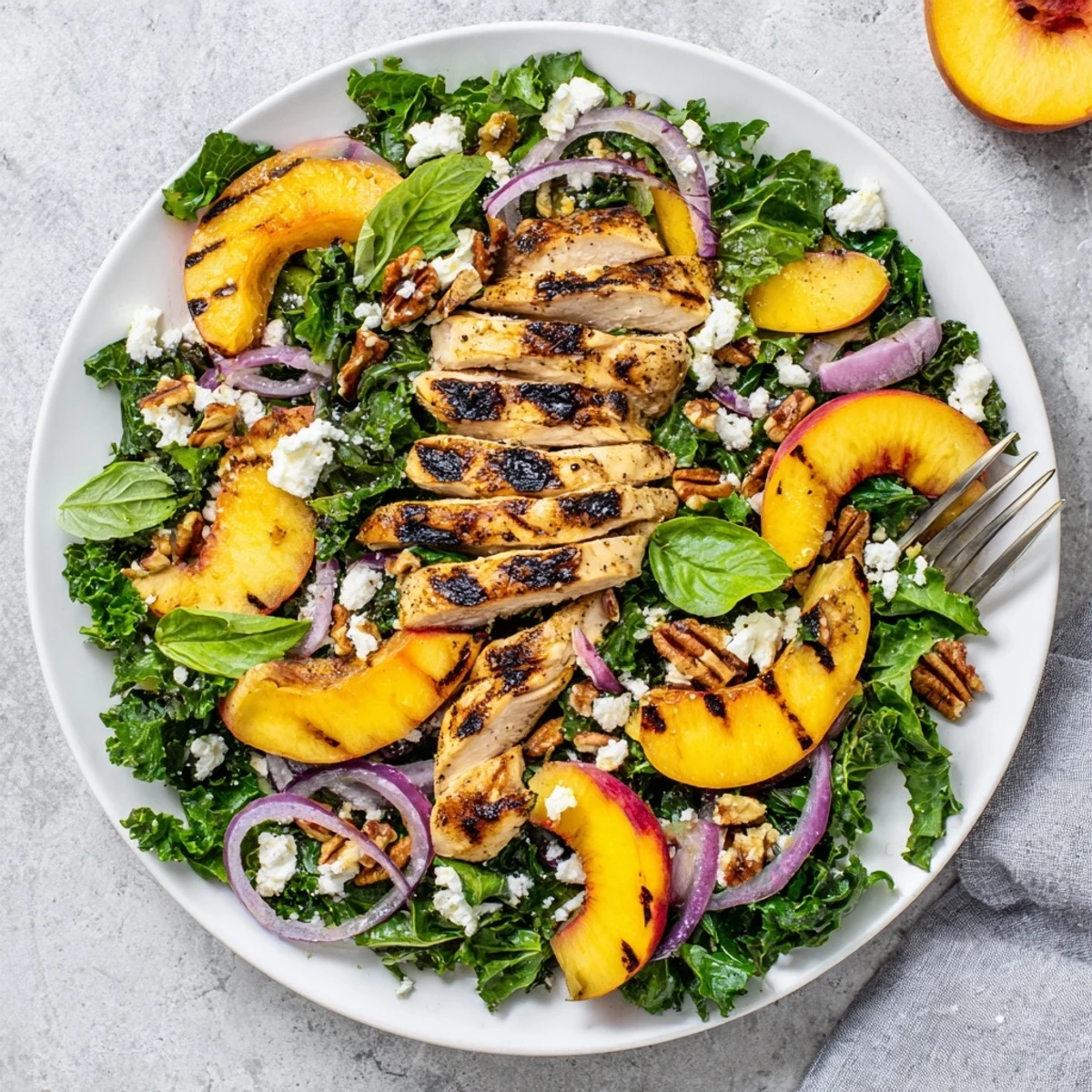Vibrant summer bowl of grilled nectarine and kale chicken salad topped with basil and toasted pecans