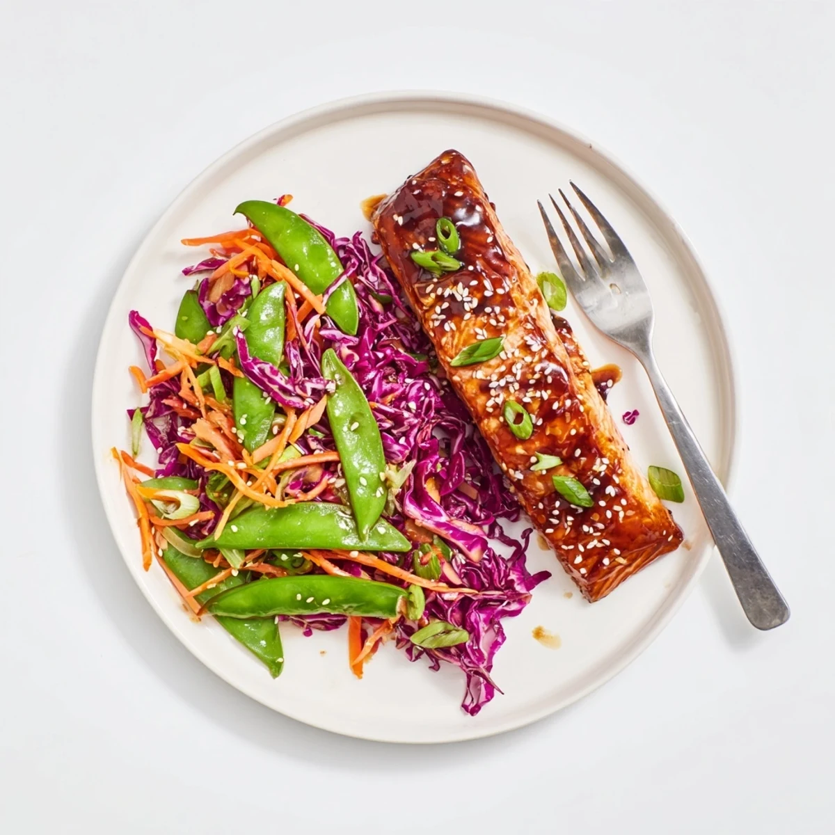 Golden glazed Miso Ginger Salmon fillets with caramelized edges resting beside a vibrant sesame snap pea slaw featuring purple cabbage and bright orange carrots