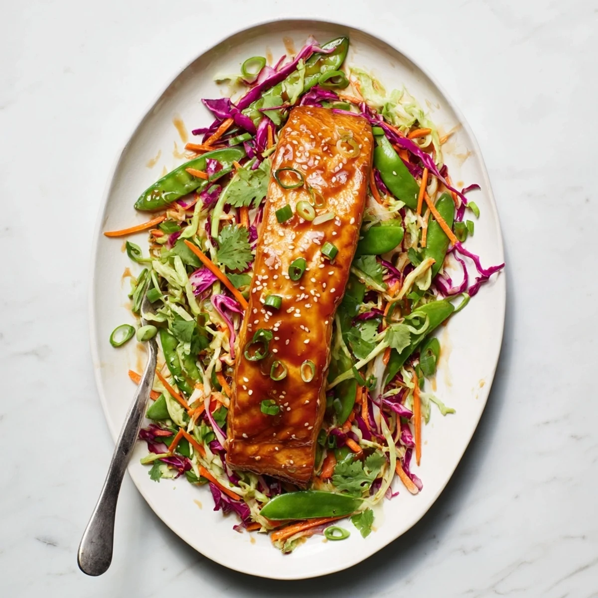 Baked salmon with shiny miso maple glaze served over crunchy purple green cabbage slaw with fresh cilantro garnish