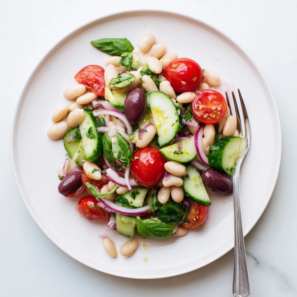 Mediterranean white bean and tomato cucumber basil salad in a white bowl with vibrant red tomatoes and green basil scattered throughout