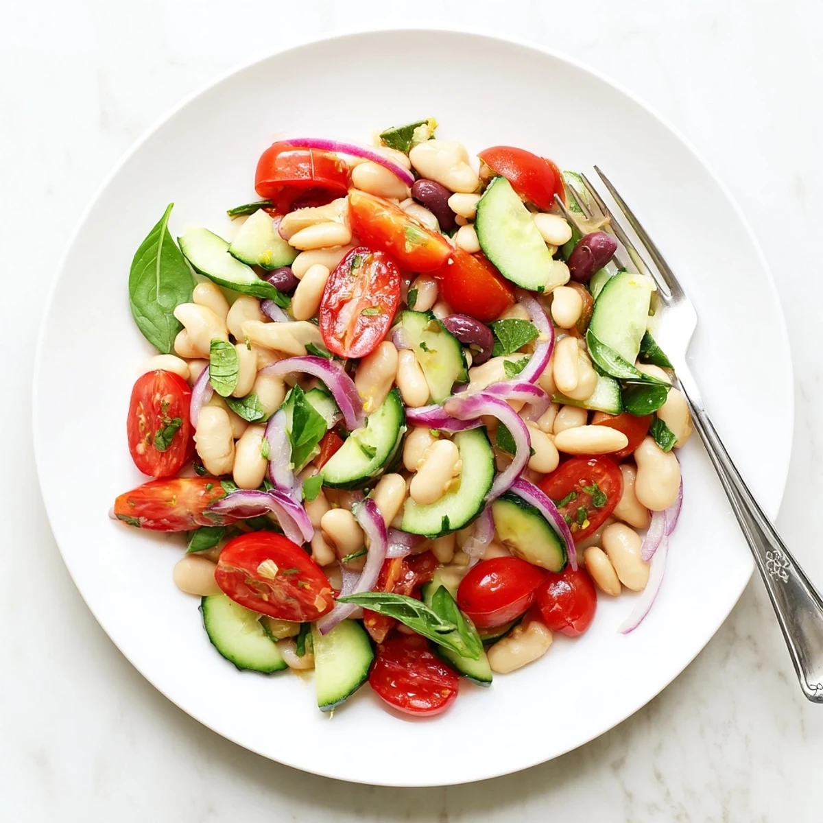 Colorful Mediterranean white bean salad featuring diced cucumbers halved tomatoes and torn basil leaves drizzled with tangy vinaigrette