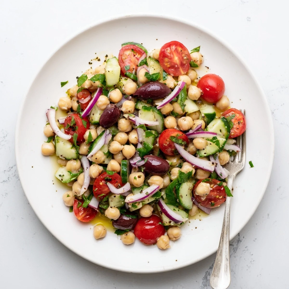 Fresh Mediterranean chickpea and tomato basil cucumber salad served in white ceramic bowl