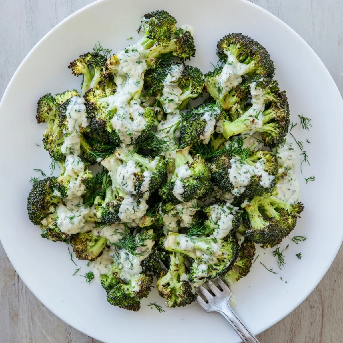 Charred tender broccoli topped with zesty tahini dressing and fresh green herbs for a Mediterranean side dish
