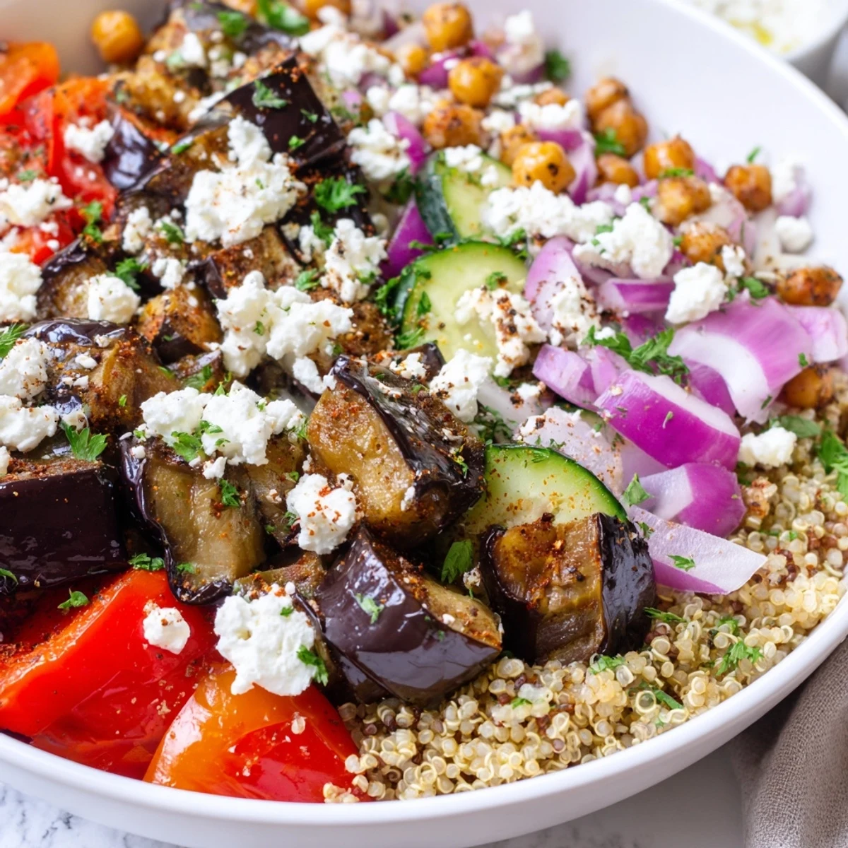 Mediterranean roasted eggplant quinoa grain bowl topped with tangy feta crumble and fresh herbs