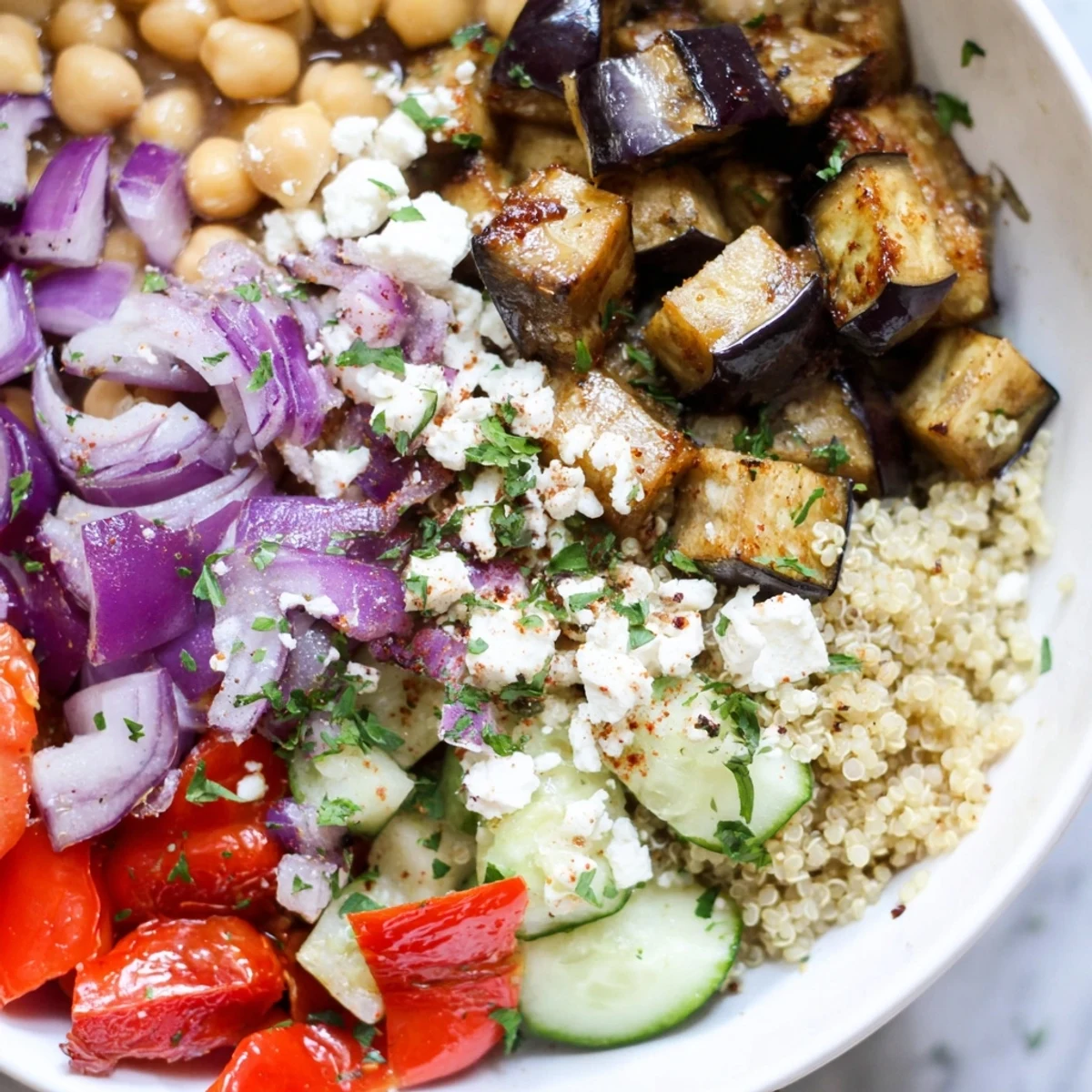 Smoky golden eggplant and fluffy quinoa grain bowl drizzled with herb dressing and crumbled feta