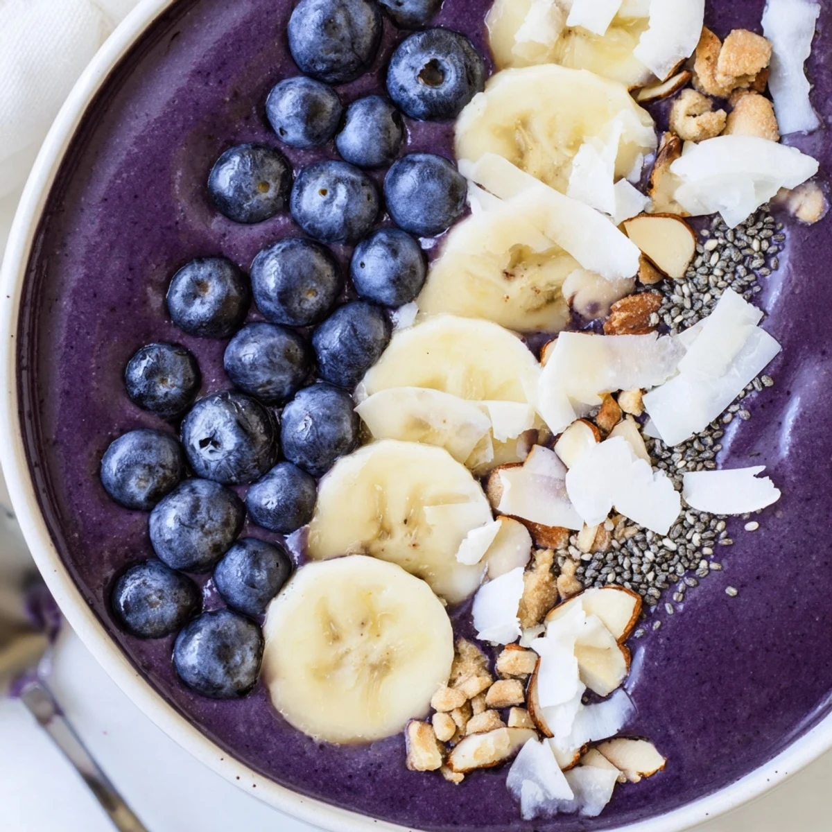 Creamy blueberry banana almond smoothie bowl topped with coconut flakes and fresh berries