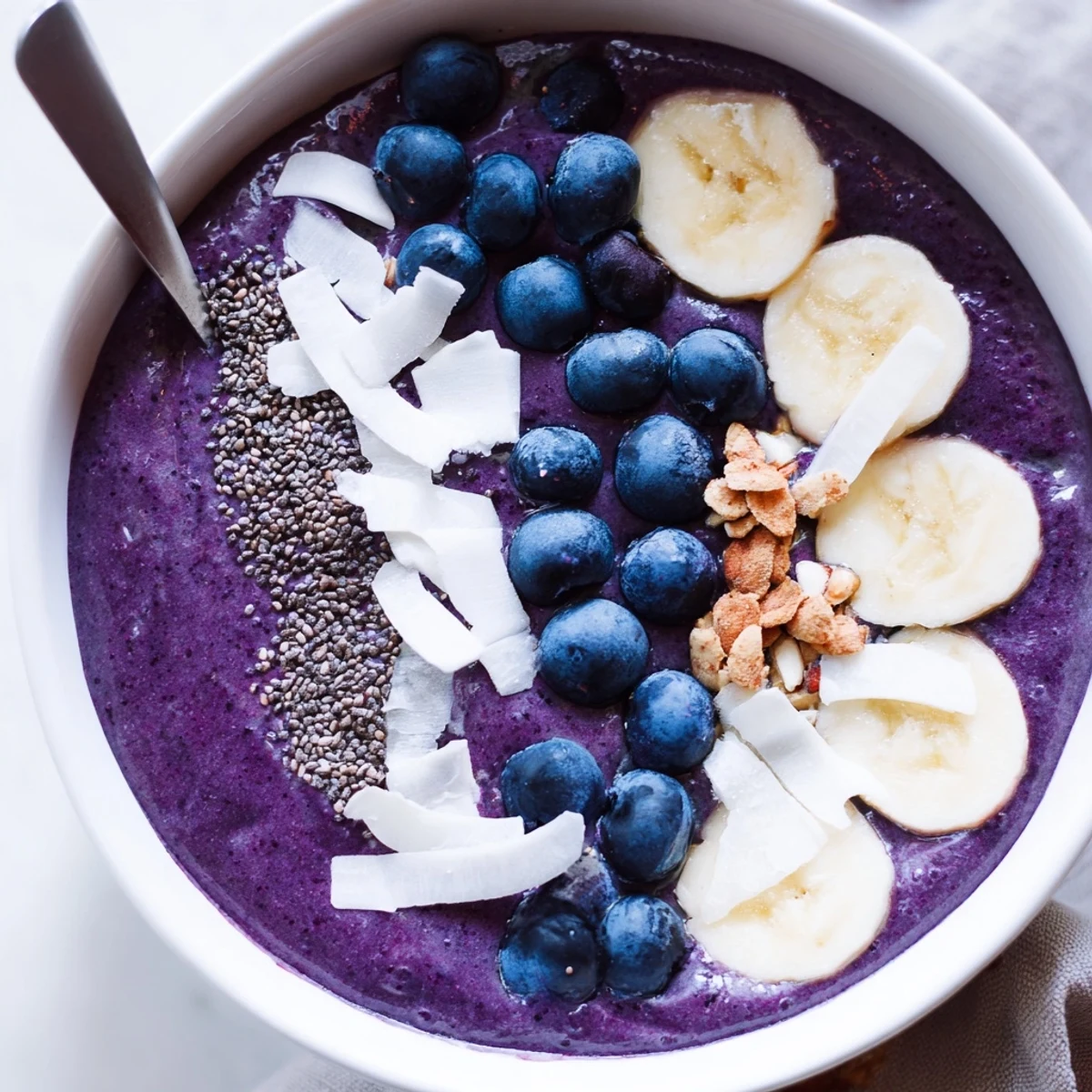 Thick purple blueberry banana almond smoothie bowl drizzled with toppings in a ceramic dish