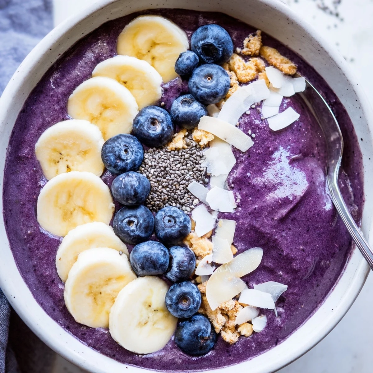 Vibrant blueberry banana almond smoothie bowl crowned with sliced bananas almonds and toasted coconut