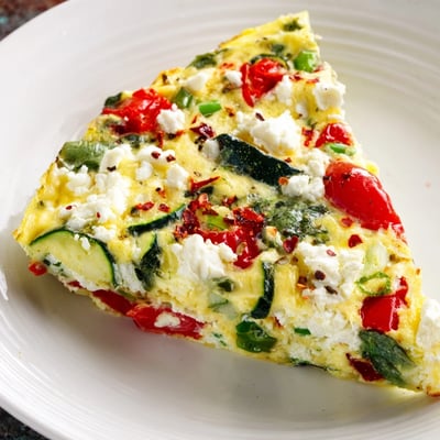 Golden sliced wedges of New Year Low Fat Frittata served on a white plate, showcasing fluffy eggs, cherry tomatoes, and green onions for a healthy breakfast.