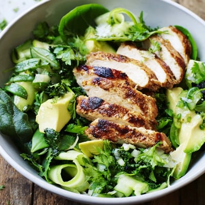 A close-up of Evergreen Paleo Salad showcases diced avocado and sugar snap peas tossed in a glistening lemon dressing.