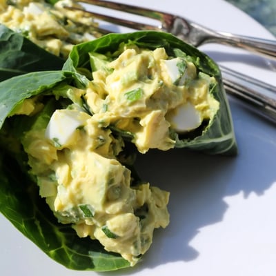 Avocado egg salad collard wraps sliced in half on a white plate showing vibrant colors.