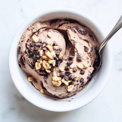 A bowl of Chocolate Peanut Butter Protein Nice Cream with a soft serve texture and fresh banana garnish.