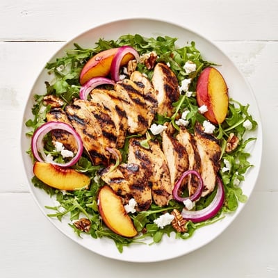 Colorful summer salad bowl featuring juicy charred nectarines atop peppery arugula and sliced chicken