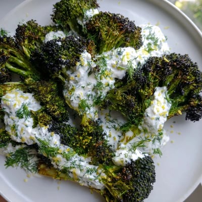 Crisp charred broccoli florets topped with creamy tangy lemon herb yogurt drizzle sauce