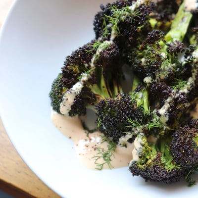 Golden roasted broccoli florets topped with creamy lemon herb tahini drizzle sauce close-up