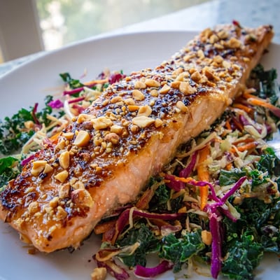 Golden glazed miso maple salmon served over crunchy rainbow sesame kale slaw on a white plate